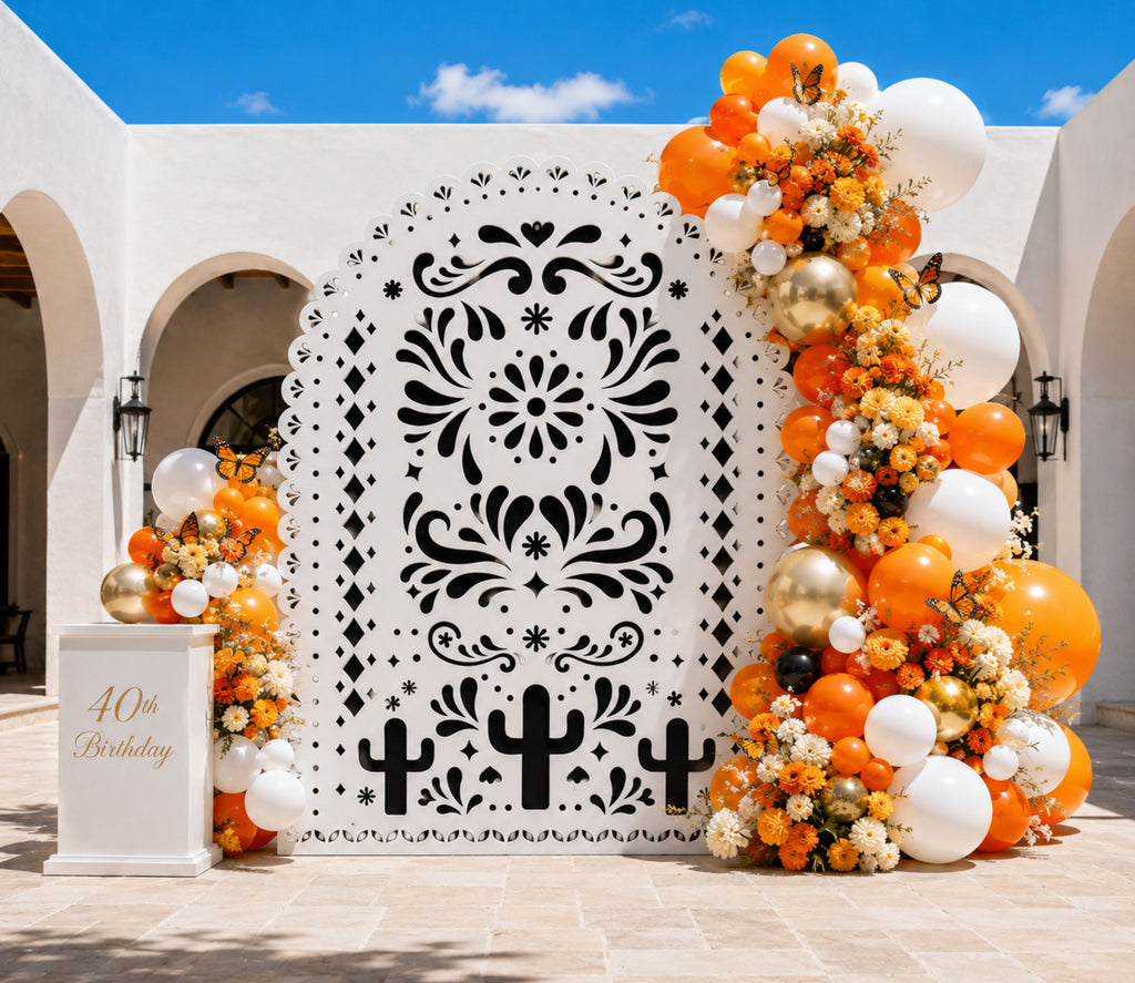 White printed papel picado backdrop with orange balloons and floral decorations for Mexican celebration